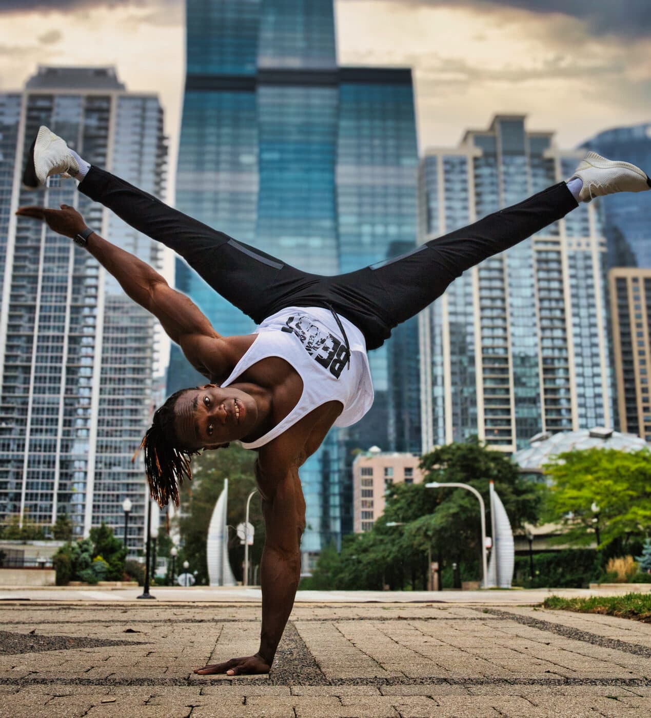 Alseny Sylla holding a one-arm handstand with legs split wide in an urban plaza