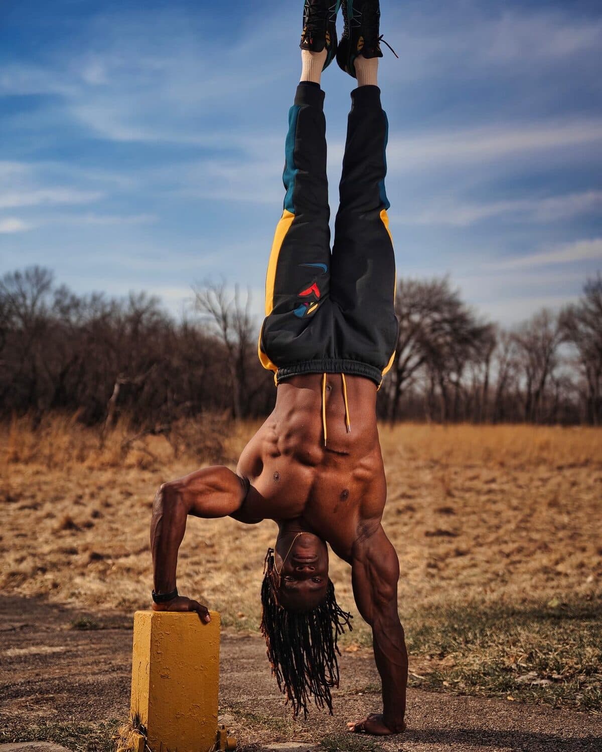 Alseny Sylla in a straddle handstand balanced on a raised block in an open field